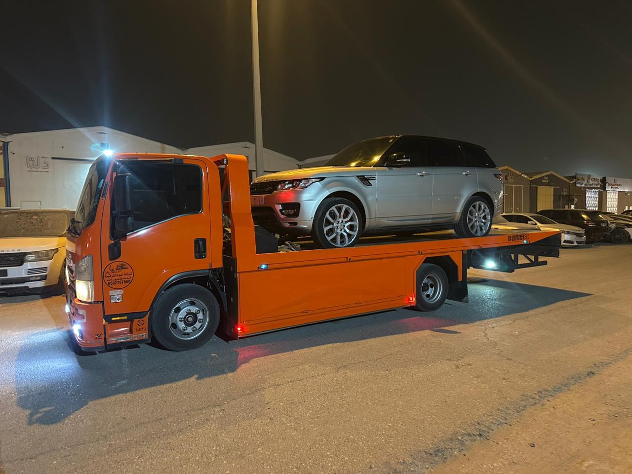 سطحة برتقالية تحمل رينج روفر فضي في الليل